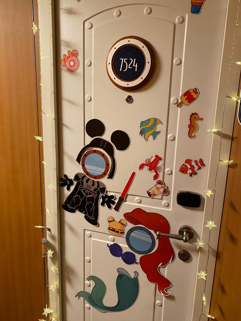 Porta de cabine decorada no cruzeiro Disney com ímãs temáticos de personagens, destacando a tradição de personalização das cabines na Disney Cruise Line.