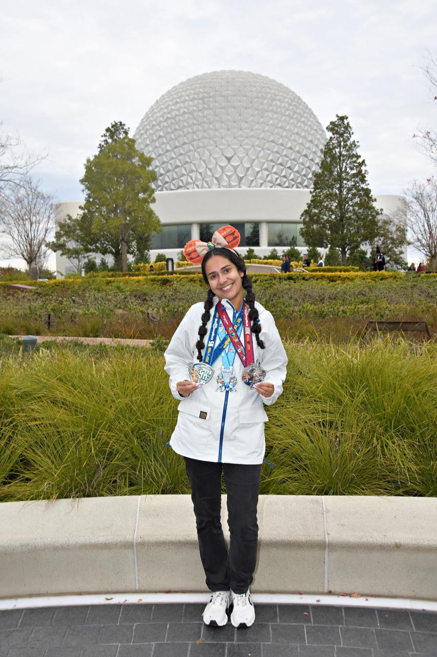Corredora exibindo medalhas da runDisney em frente à Spaceship Earth, no EPCOT, durante viagem para participar das corridas Disney em Orlando