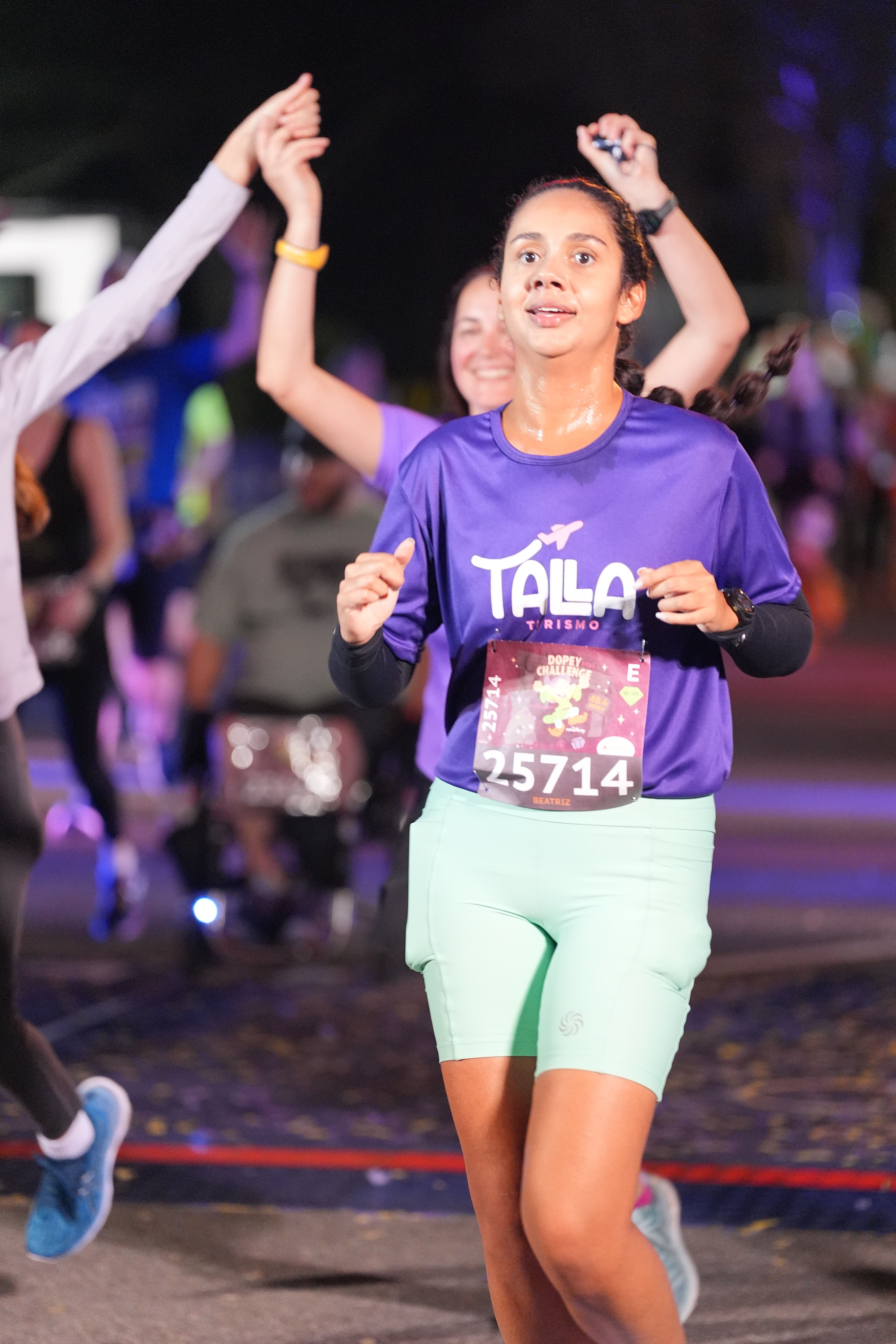 Beatriz da Talla Turismo próxima a linha de chegada de uma prova runDisney durante o Dopey Challenge no Walt Disney World, em Orlando, usando camiseta roxa da agência e número de peito oficial da corrida