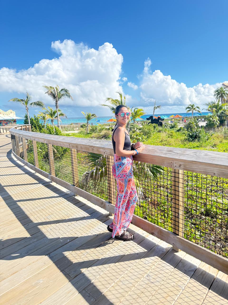 Beatriz da Talla Turismo na Lookout Cay at Lighthouse Point, ilha privativa da Disney nas Bahamas, com passarela de madeira, coqueiros e mar azul ao fundo.