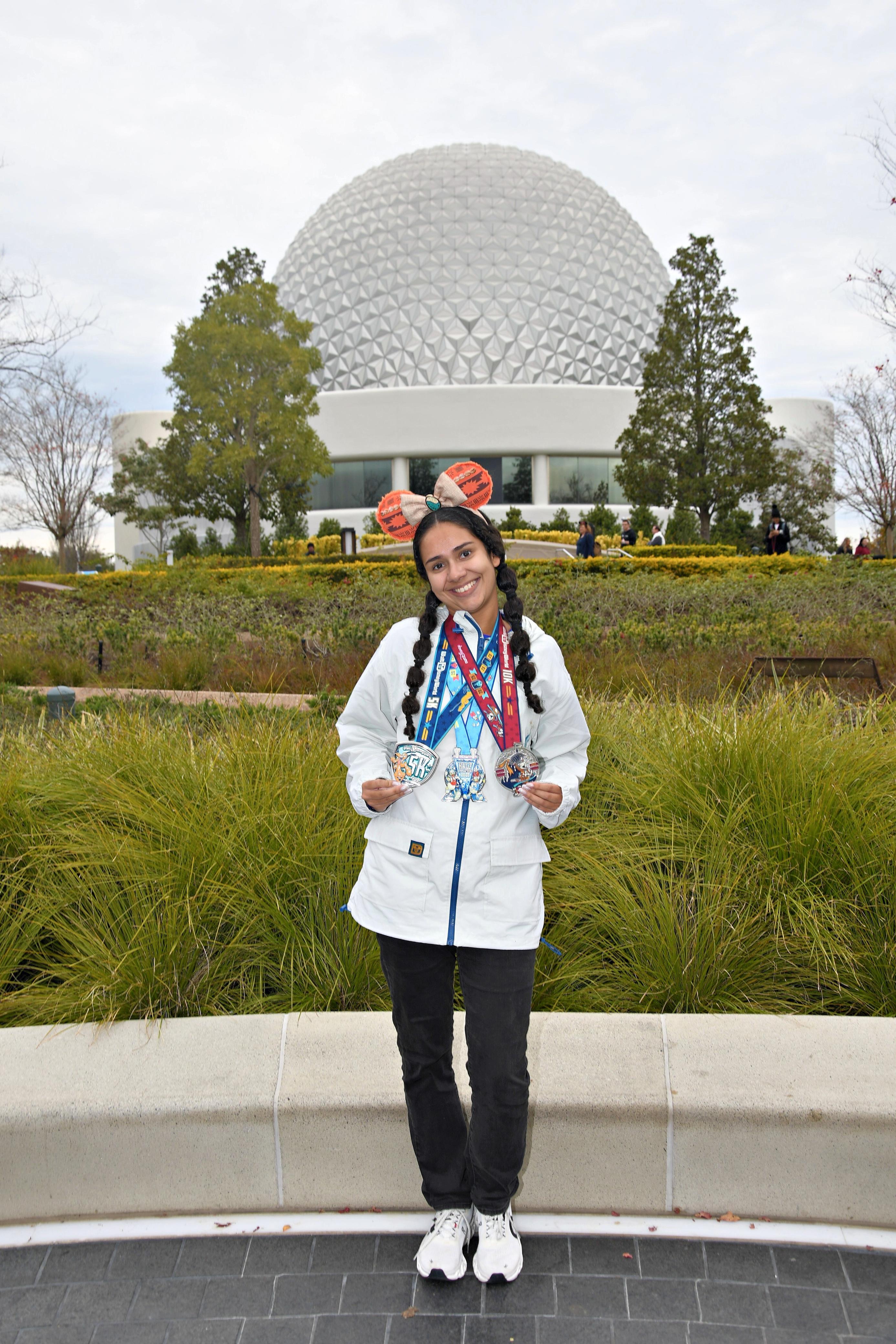 Beatriz, da Talla Turismo, usando medalhas das corridas runDisney em frente à Spaceship Earth, no EPCOT, durante a viagem a Orlando